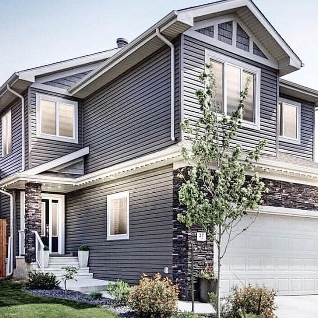 A house with a garage door and trees in front of it.