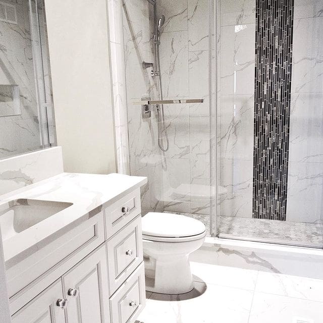 A bathroom with white cabinets and marble walls.