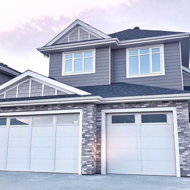 A large grey house with two white garage doors.